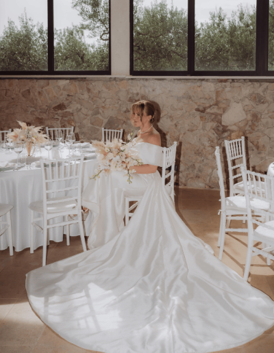 Bride sitting in an elegant reception venue during her wedding in Croatia, holding a bouquet and wearing a long satin gown.