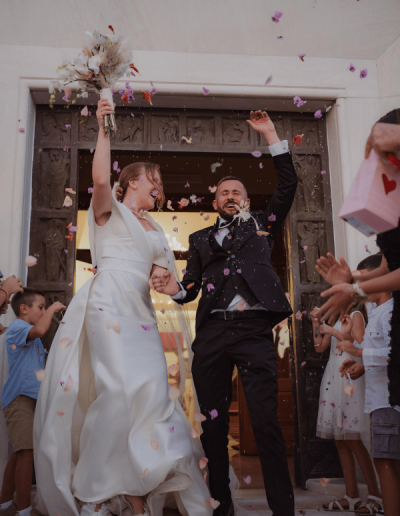 Bride and groom celebrating after their wedding ceremony in Croatia, surrounded by guests throwing petals.